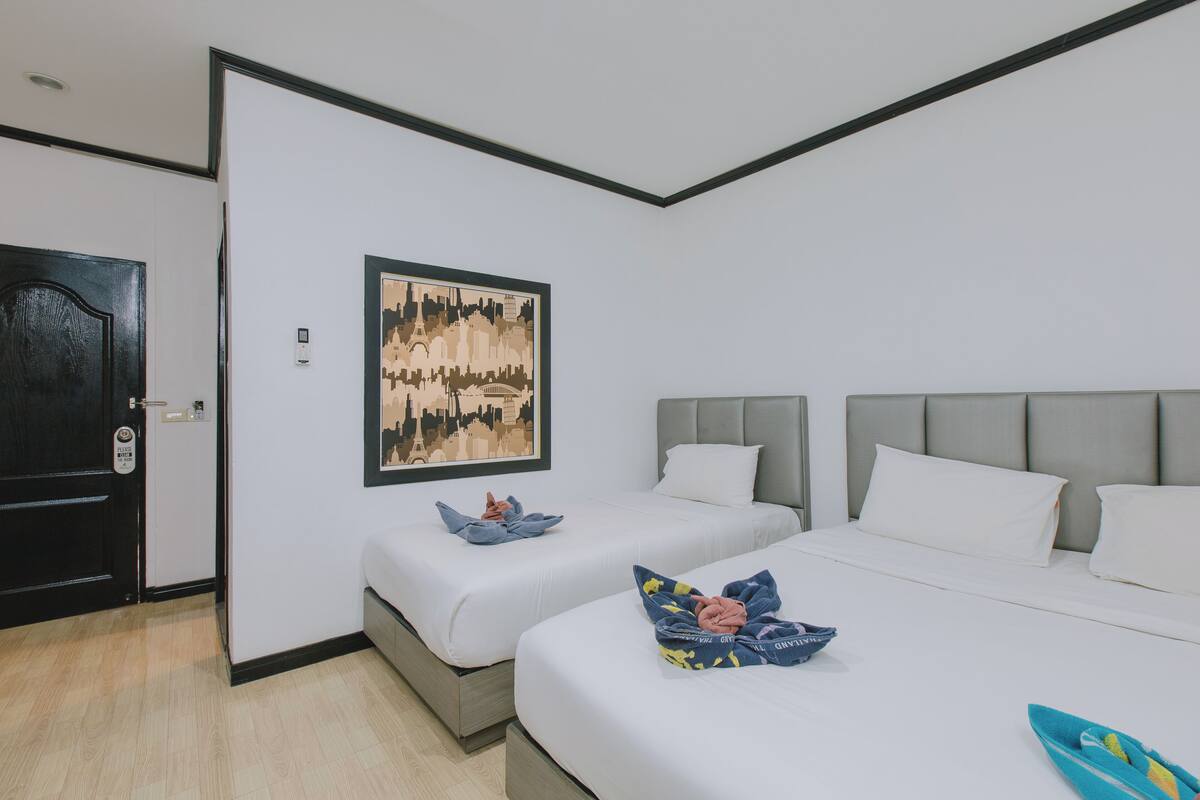 A hotel room with two beds, a door, a wall-mounted artwork, and a light switch.