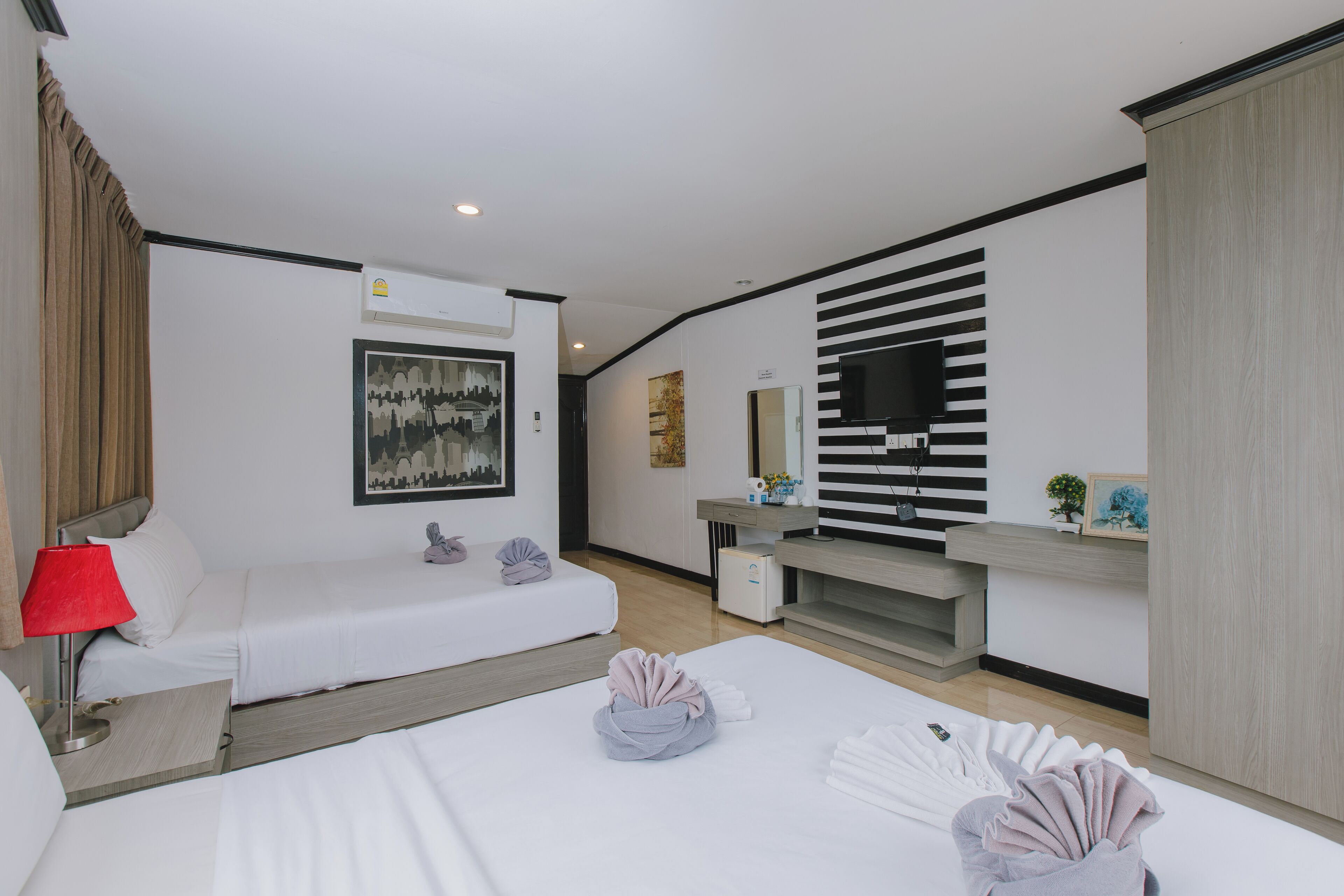 A hotel room with two beds, a desk, a mirror, and a TV.