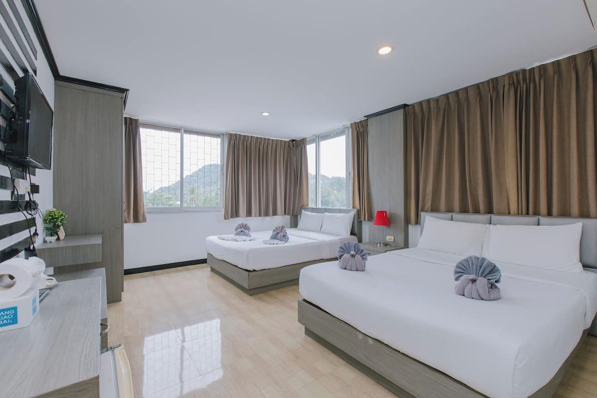 A hotel room with two beds, a desk with a computer, a TV, and a window with curtains.