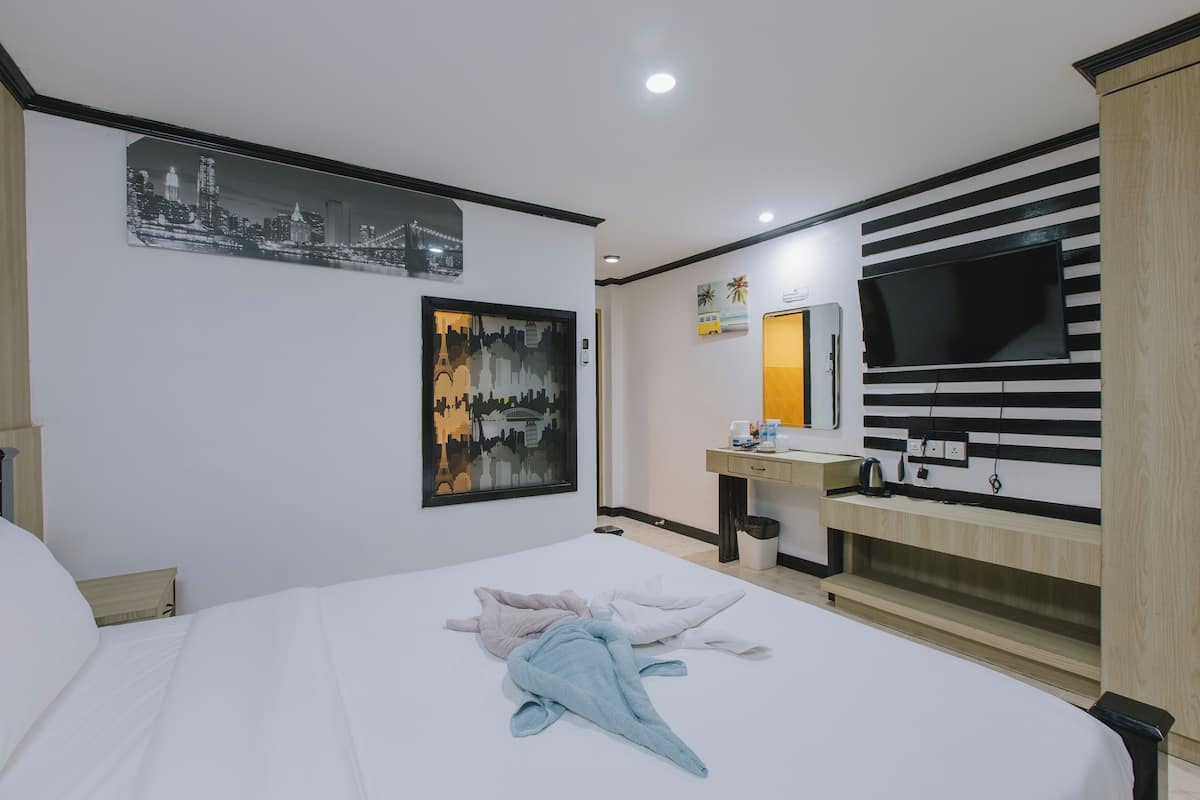 A hotel room with a large bed, a desk with a flat-screen TV, and artwork on the walls.