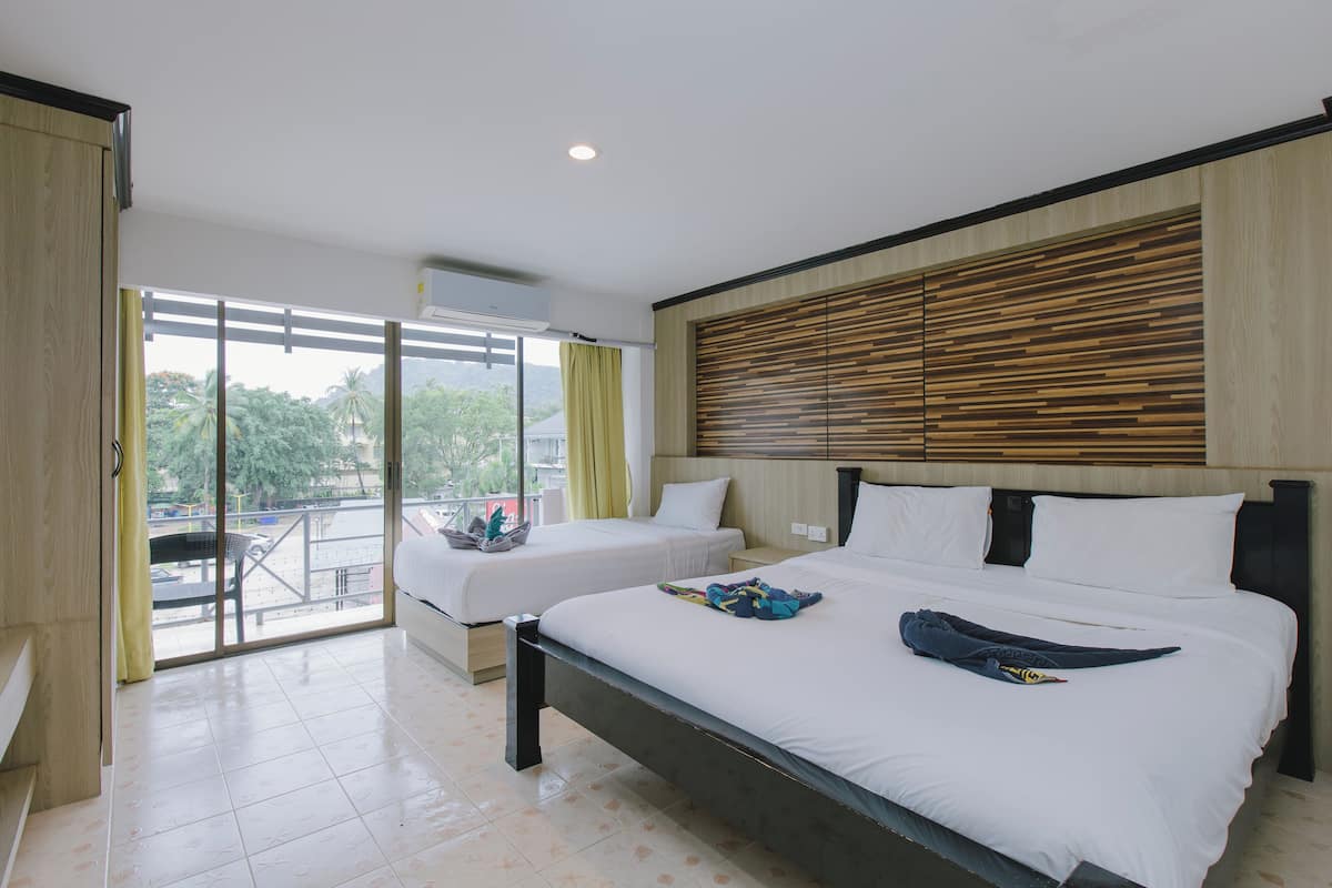 A hotel room with two beds, a balcony with a table and chairs, and a view of greenery outside.
