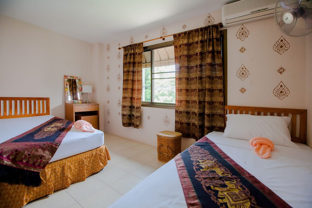 Habitación de hotel con dos camas, una ventana con cortinas, un espejo, una mesita de noche y un equipo de aire acondicionado.