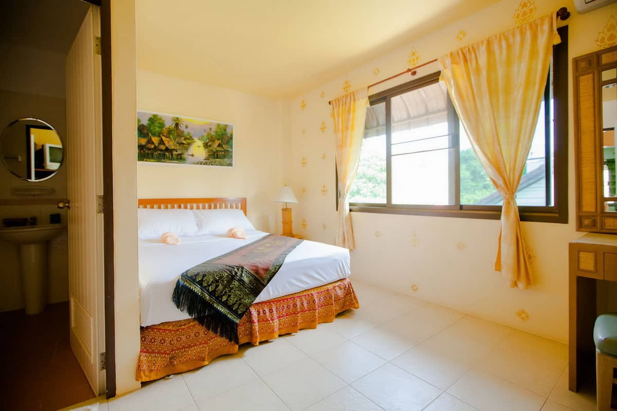Un dormitorio con cama, ventana con cortinas, mesita de noche, lámpara, un cuadro en la pared y un espejo.
