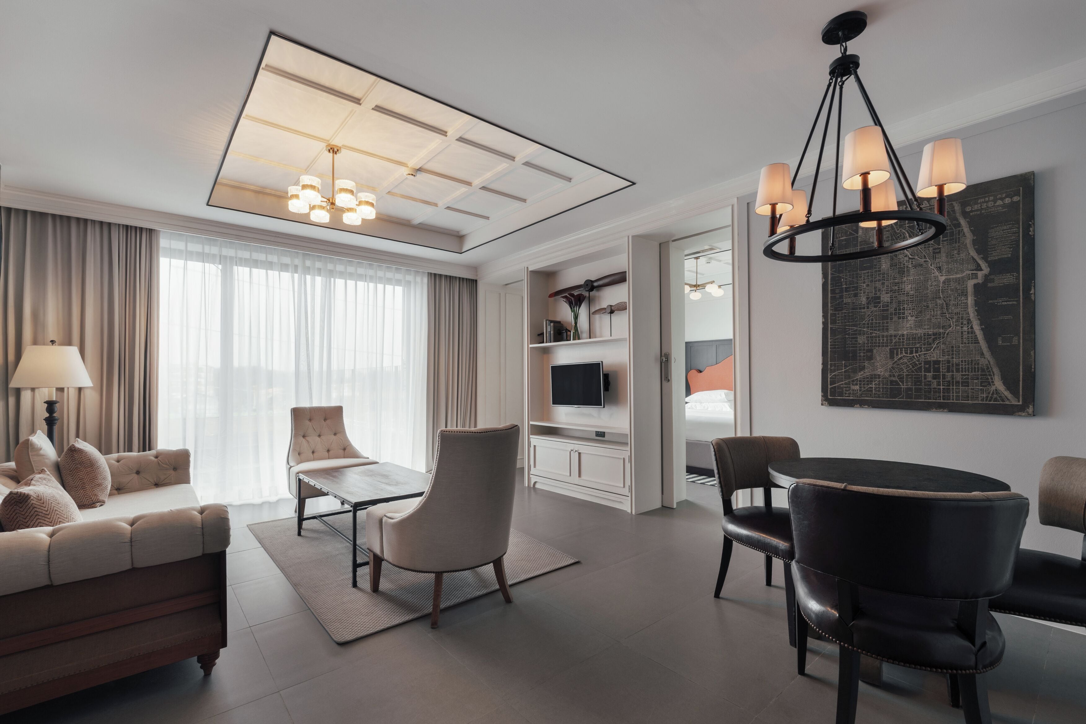 A modern hotel room with a sofa, armchairs, a dining table, and a TV.