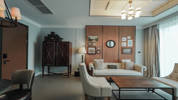 A modern hotel room with a sofa set, a wooden cabinet, a dining table, and a chandelier.