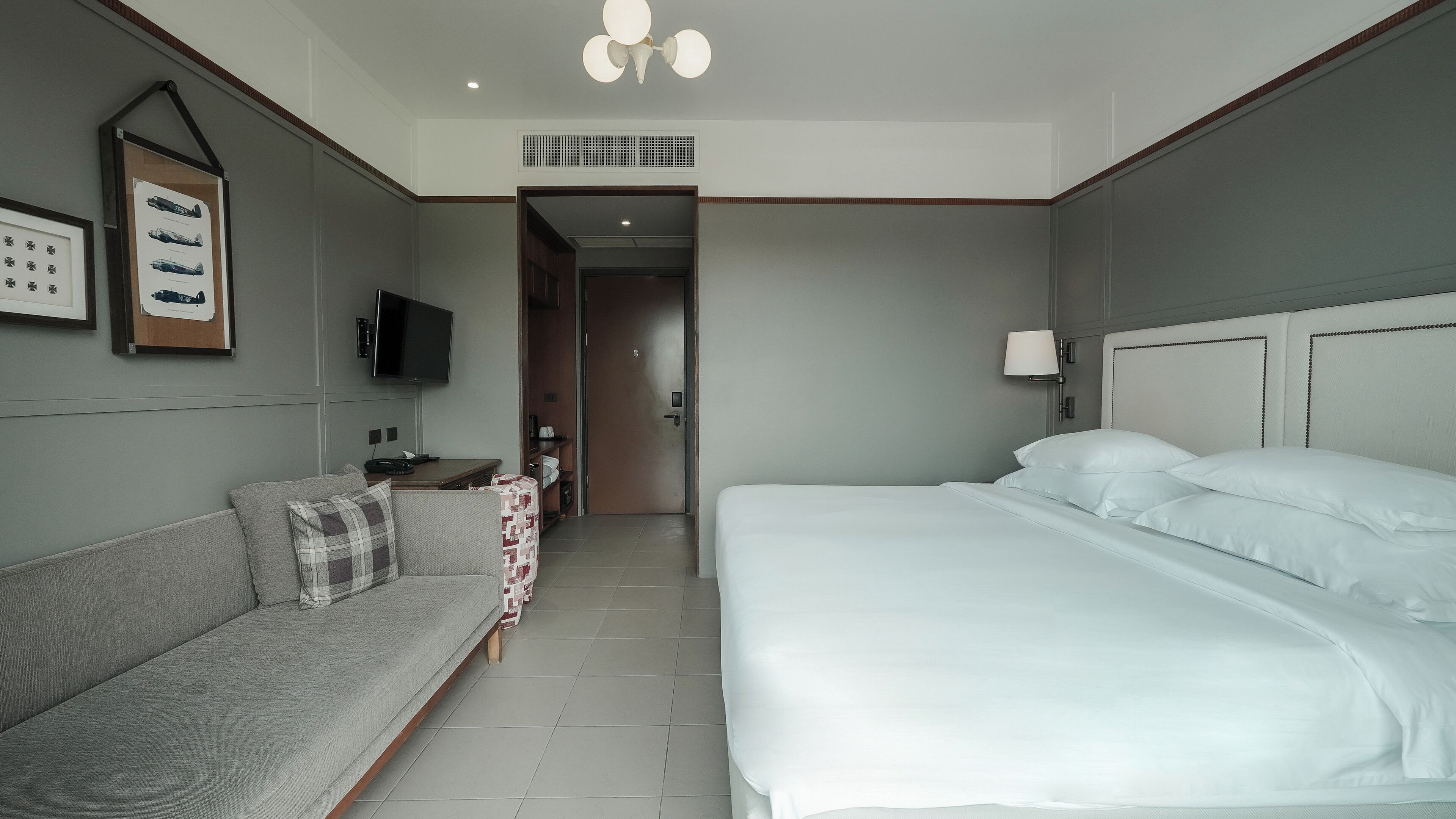 Una habitación de hotel con cama, sofá, televisor y lámpara de pared.