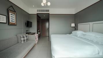 Una habitación de hotel con cama, sofá, televisor y lámpara de pared.