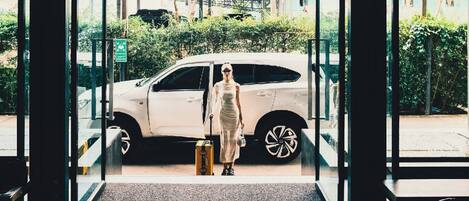 Una persona in piedi all'ingresso di un edificio, con un'auto bianca parcheggiata all'esterno.
