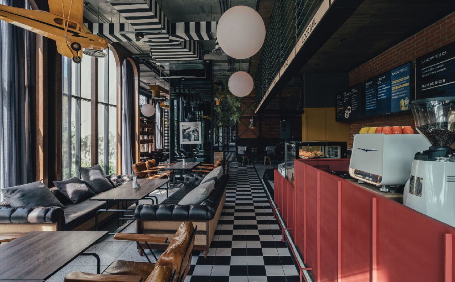 L’intérieur d’un restaurant avec un sol à carreaux, un espace salon avec des canapés et des tables, un comptoir avec une machine à café et un tableau affichant le menu.