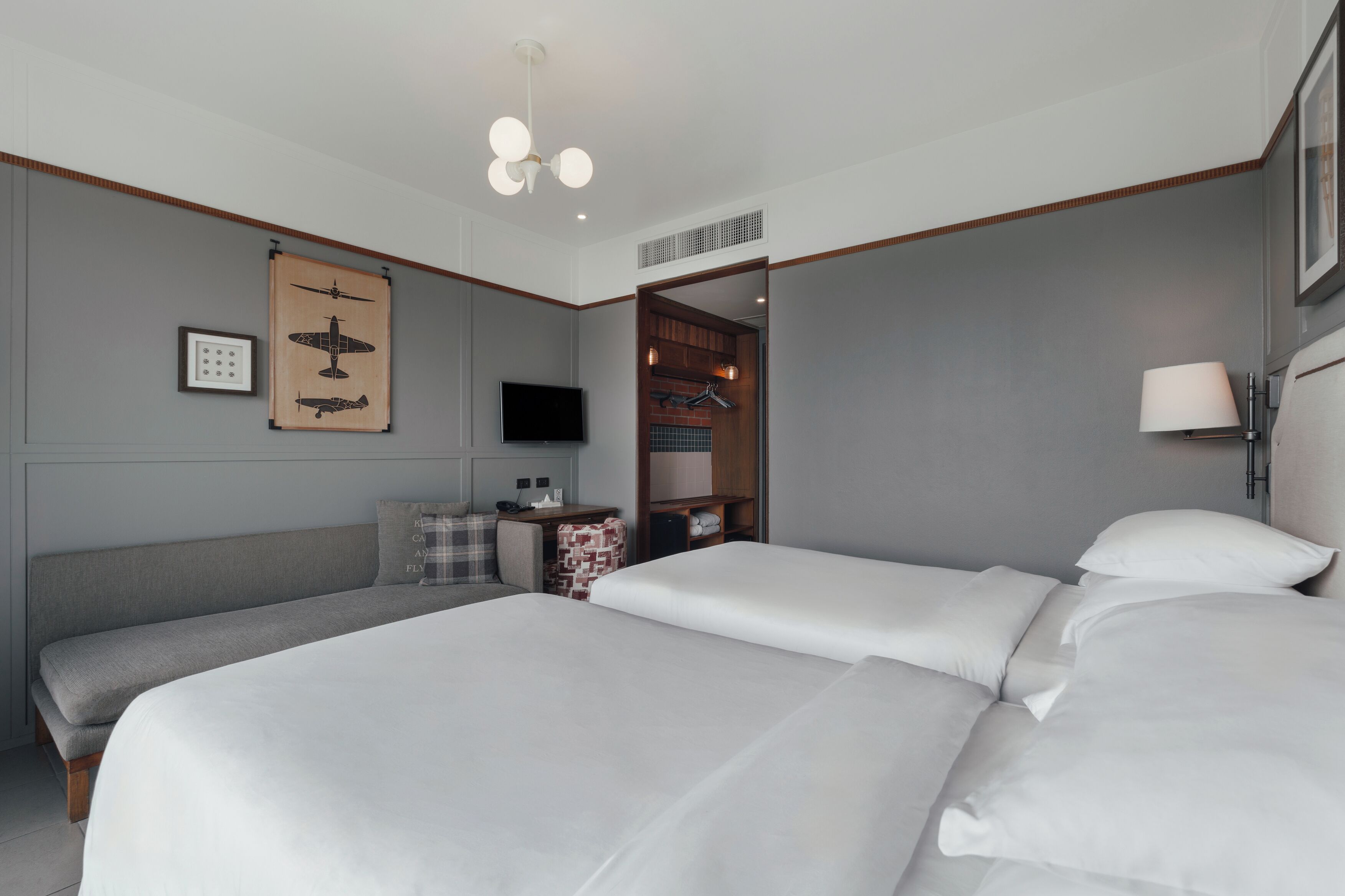 Une chambre d’hôtel avec deux lits, une télévision, une armoire en bois et un luminaire au plafond.