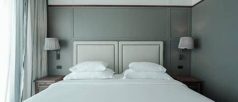 A neatly made bed with white linens and pillows, two bedside tables with lamps, and a large window with curtains.