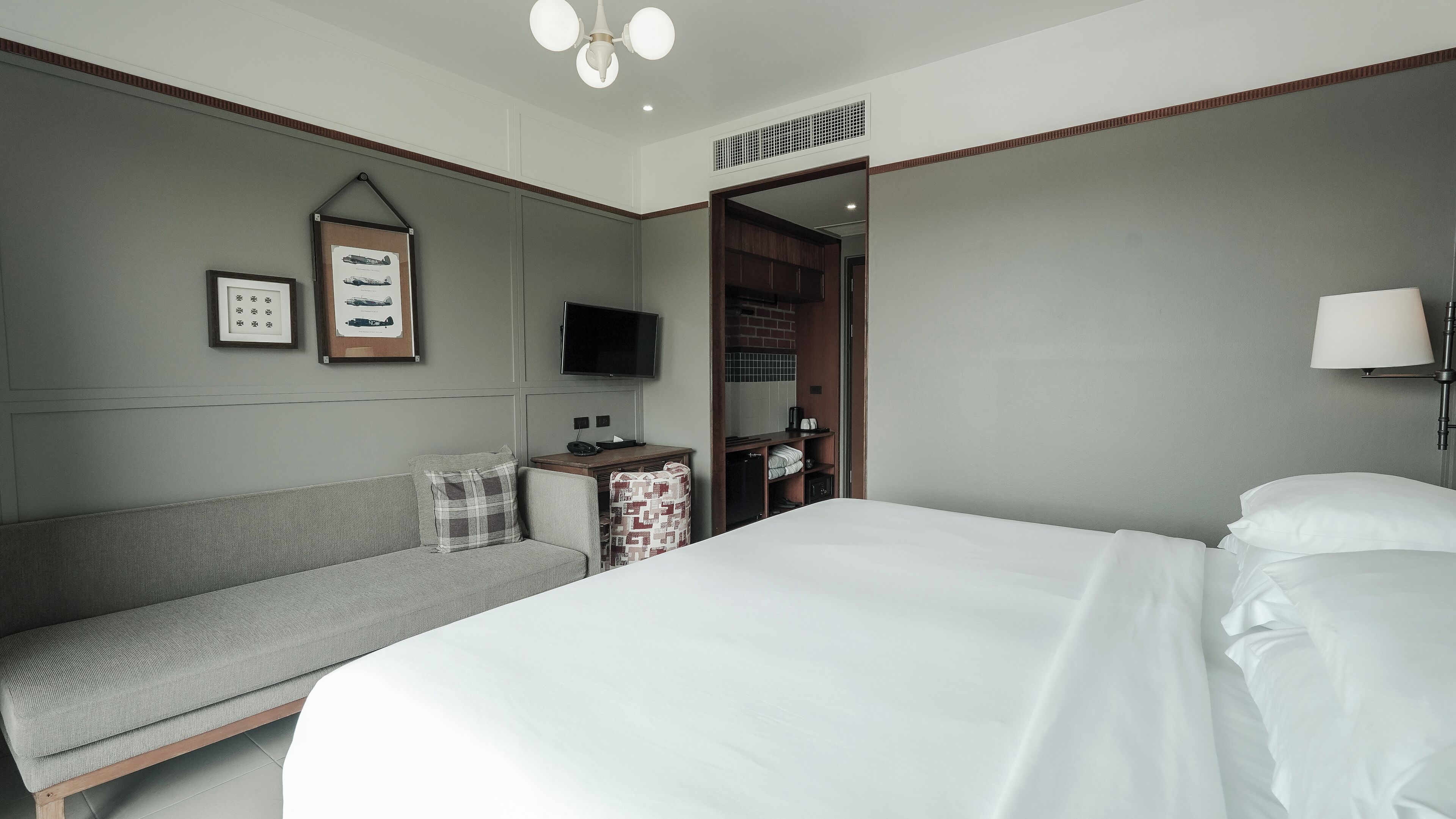 Habitación de hotel con una cama grande, un sofá, un televisor y una mesita de noche con lámpara.