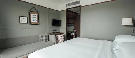 Habitación de hotel con una cama grande, un sofá, un televisor y una mesita de noche con lámpara.