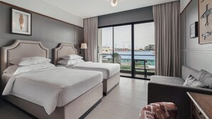 A hotel room with two beds, a sofa, a large window with a view, and a chandelier. - Sugar Marina Hotel - AVIATOR - Phuket Airport (Sa Khu)