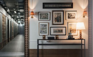 A hallway with framed pictures on the wall, a console table with a lamp, and a patterned wall design.