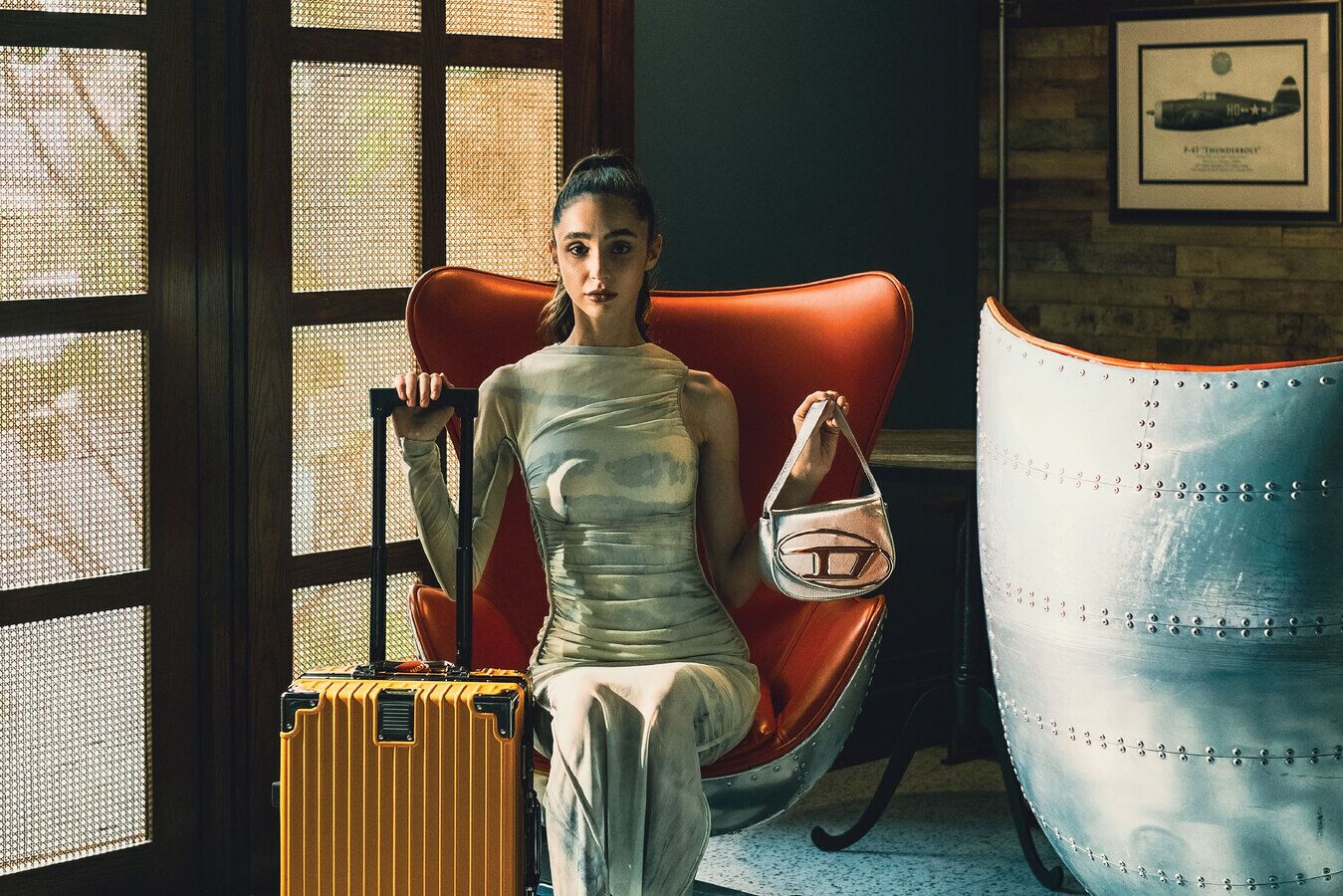 Una persona sentada en un sillón rojo de cuero con una maleta y un bolso a un lado.