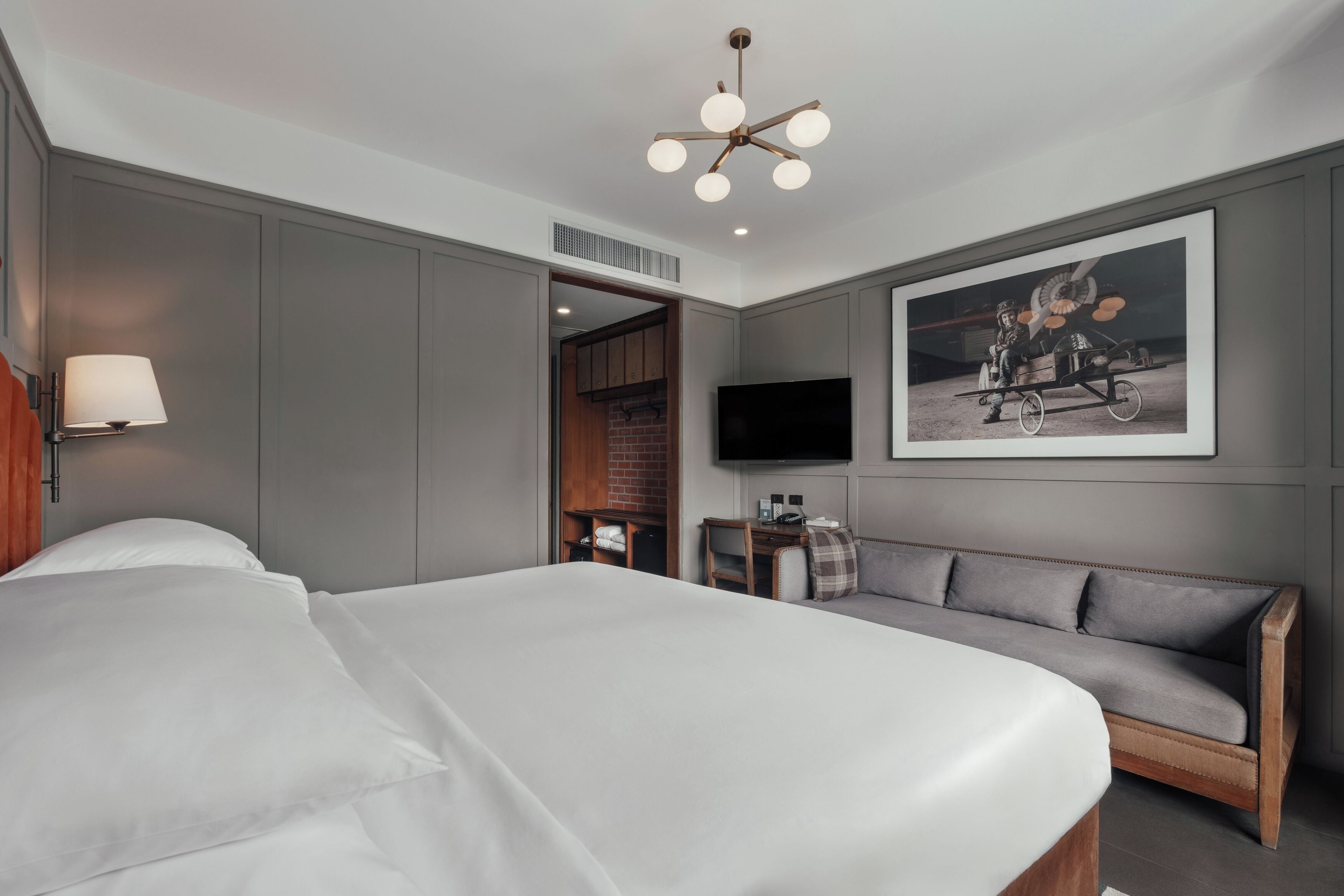 Ein Hotelzimmer mit einem großen Bett, einem grauen Sofa, einem Flachbildfernseher und einem gerahmten Bild an der Wand.