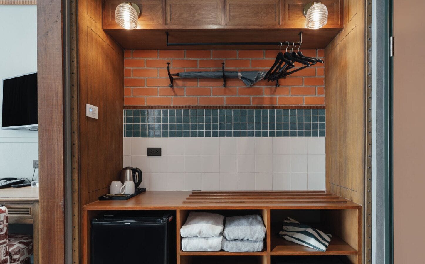 Een kleine keuken met een backsplash van baksteen, een kleine koelkast en een plank met handdoeken.