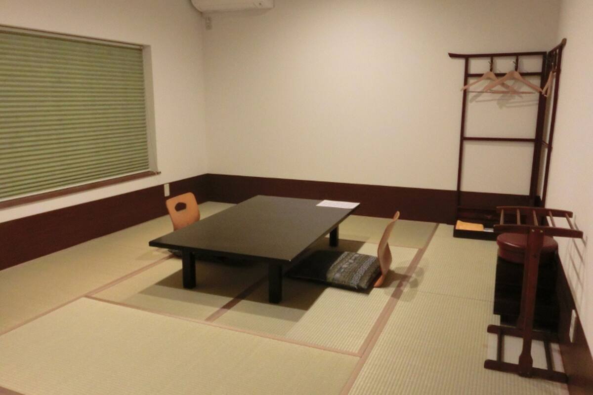 A tatami mat room with a low table, a chair, a wooden bench, and a shelf with hangers.