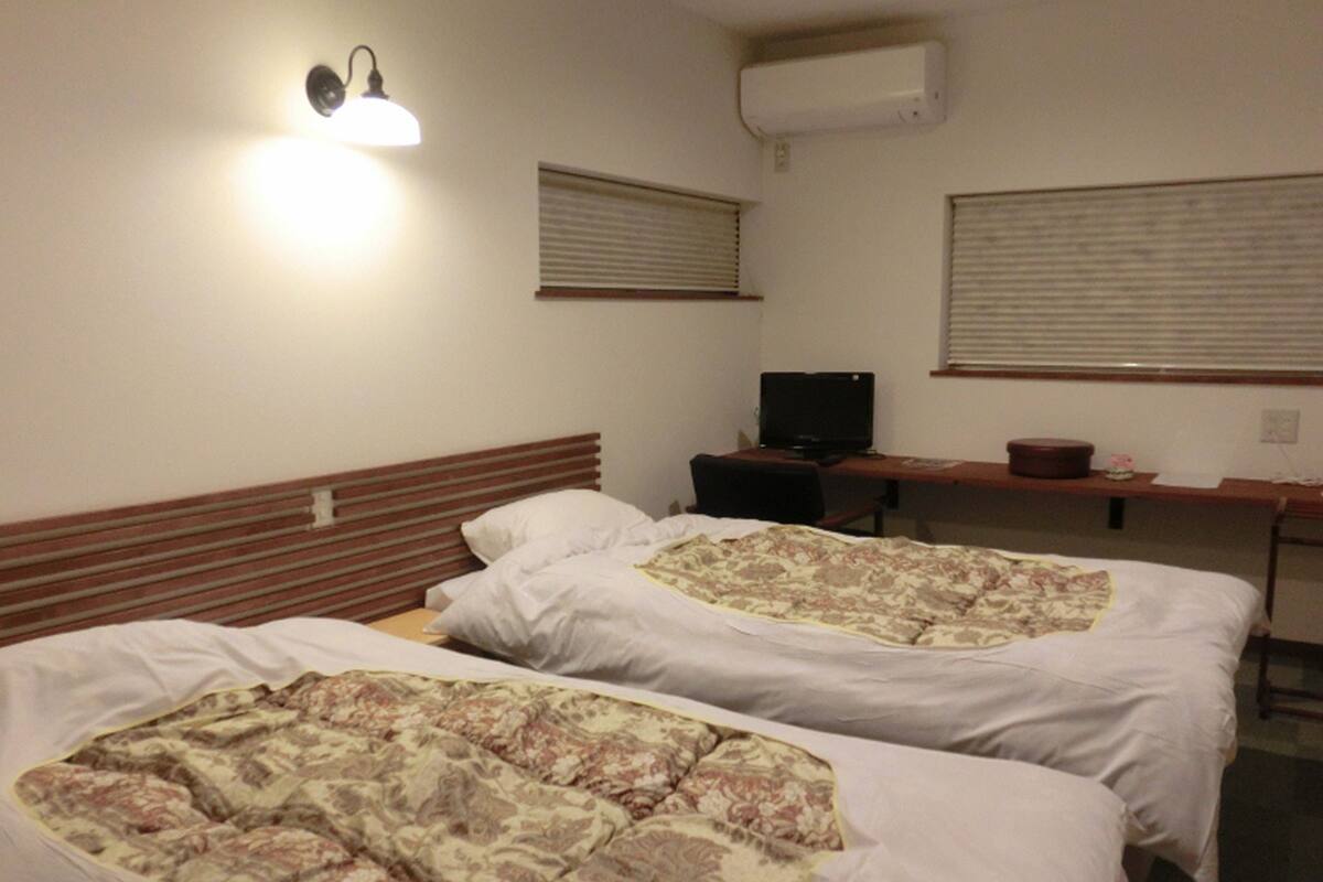 A hotel room with two beds, a desk with a computer, and an air conditioning unit on the wall.