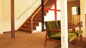 A spacious room with a wooden staircase, a green upholstered chair, and a wooden coffee table. - Yourou Onsen Honkan (Onomichi)