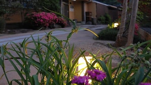 A building with a yellow facade, a paved entrance, and a garden with pink flowers and green plants. - Yourou Onsen Honkan (Onomichi)