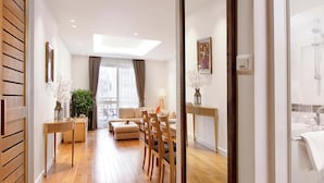 Ein modernes Hotelzimmer mit Holzboden, einer Couch, einem Esstisch, Stühlen und einem großen Spiegel, der den Raum reflektiert.
