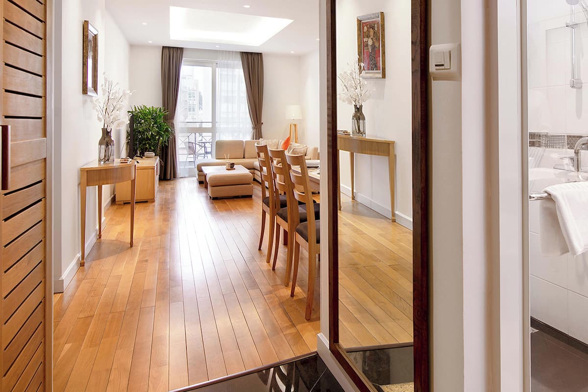 Une chambre d’hôtel moderne avec un plancher en bois, un canapé, une table à manger, des chaises et un grand miroir qui reflète la pièce.