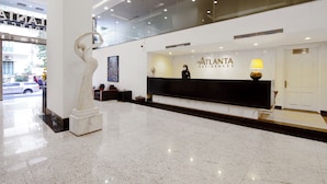 Ein Hotel-Empfangsbereich mit Marmorboden, einer Rezeption, einer großen Skulptur und einem gerahmten Kunstwerk.