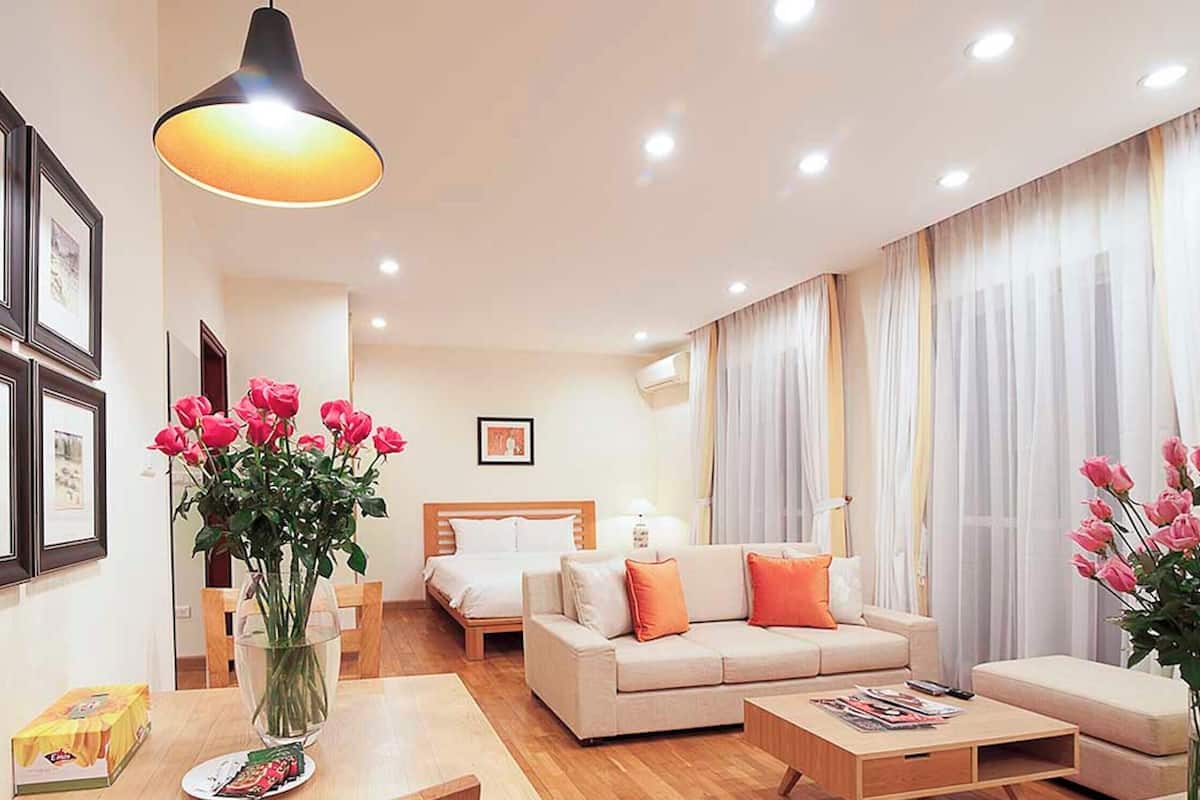 Une chambre d’hôtel avec un lit, un canapé, une table basse, un vase avec des fleurs, des tableaux encadrés au mur et un luminaire suspendu.