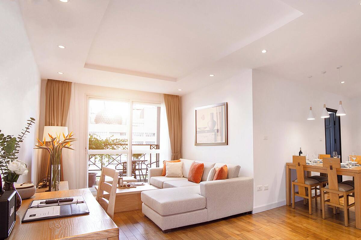 Un salon moderne avec un canapé, une table à manger et des chaises. Il y a une fenêtre avec des rideaux, une lampe et un tableau encadré au mur.
