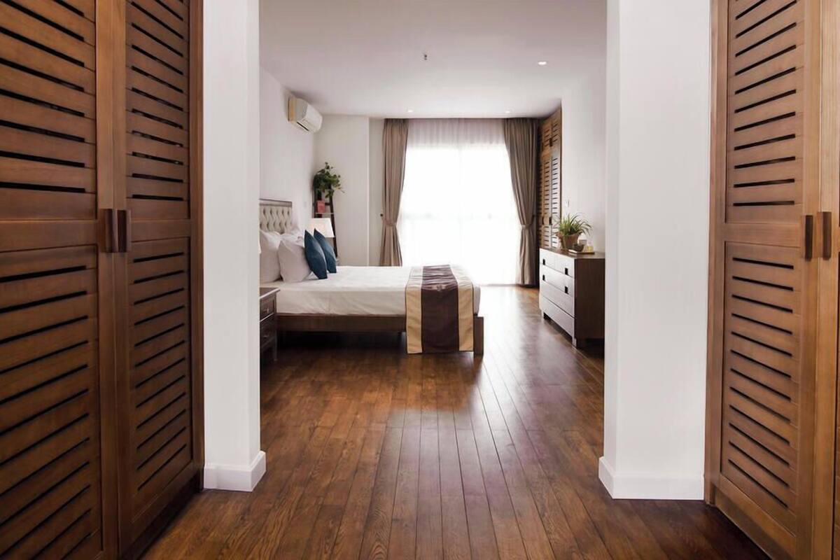 Une chambre à coucher avec un lit, des tables de chevet, une commode et une fenêtre avec des rideaux.