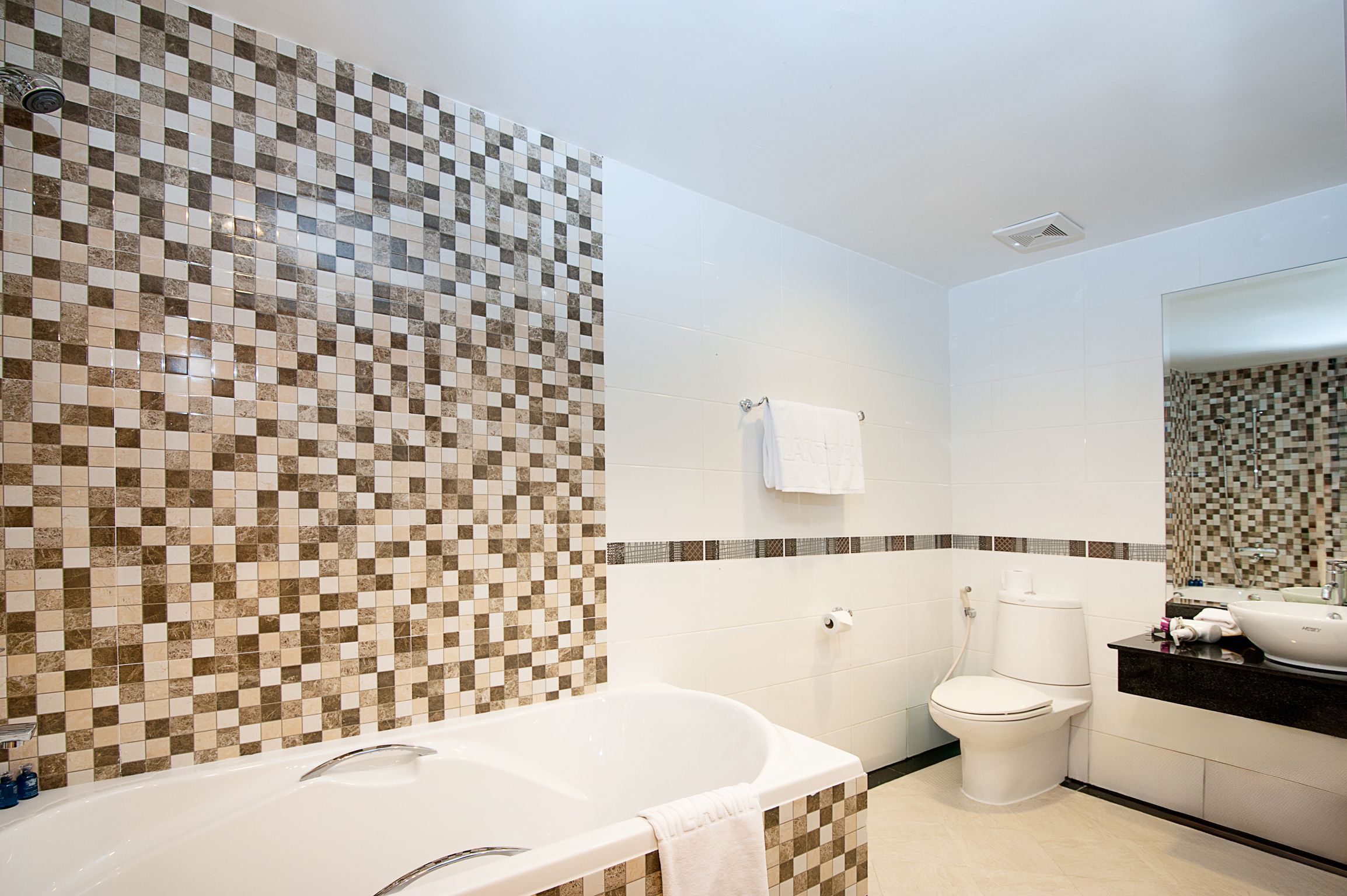 A bathroom with a checkered tile wall, a white bathtub, a toilet, and a mirror.