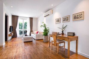 Una sala de estar moderna con piso de madera, un sofá, una mesa de comedor con sillas, un televisor y obras de arte en la pared.