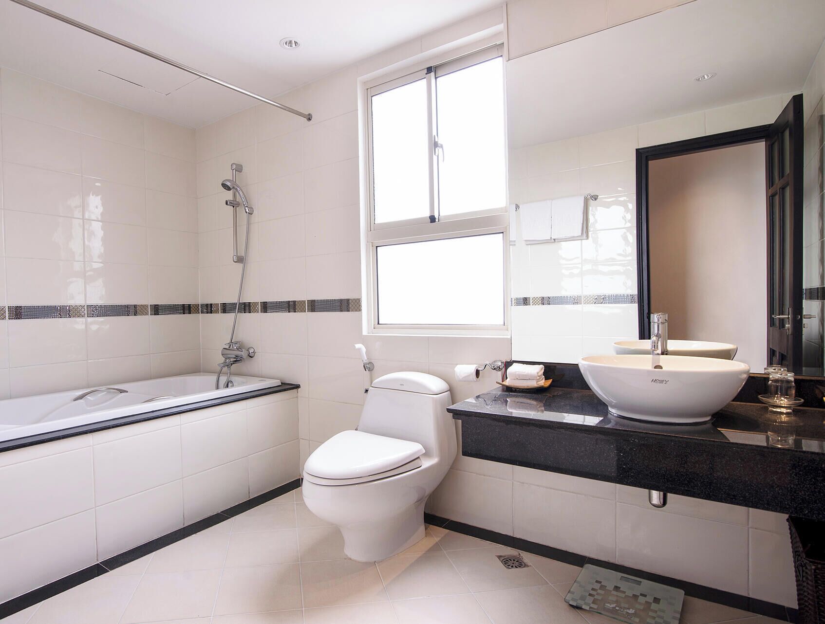 A modern bathroom with a bathtub, toilet, and sink, featuring a large window and a mirror.