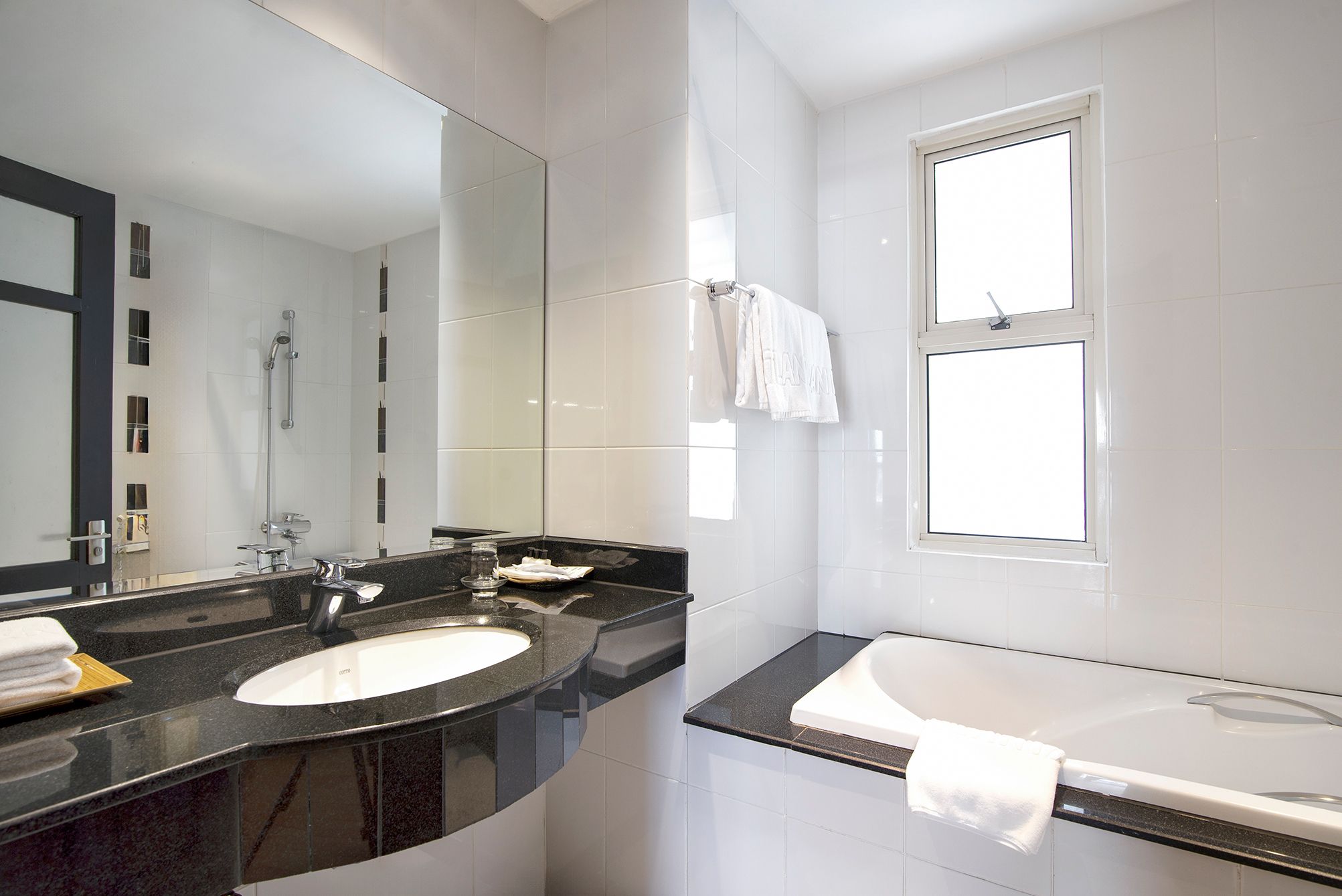 Une salle de bain moderne avec un grand miroir, deux lavabos, une baignoire et une fenêtre.