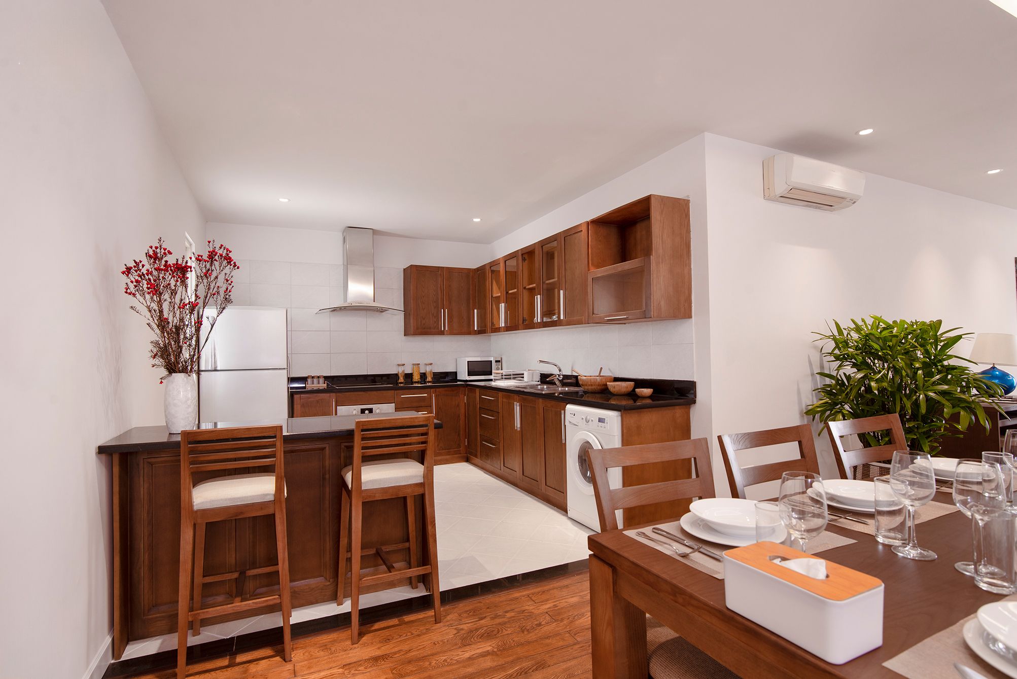 A modern kitchen with wooden cabinets, a dining area with a table set for four, and a built-in oven.