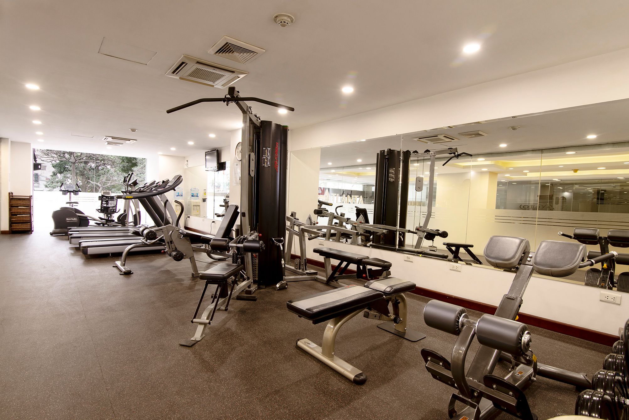 Un gimnasio con diverso equipo de ejercicio, un espejo grande y vistas al exterior.