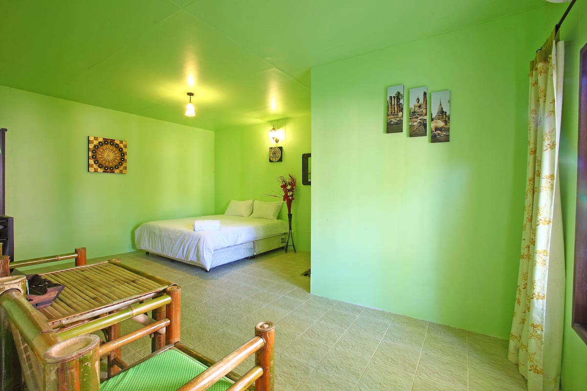 A room with a bed, a small table, and a chair. There are wall decorations and a curtain.