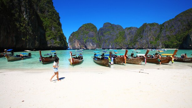 A beach with boats and a person walking. - PP Red Tuna Hut (Ko Phi Phi)