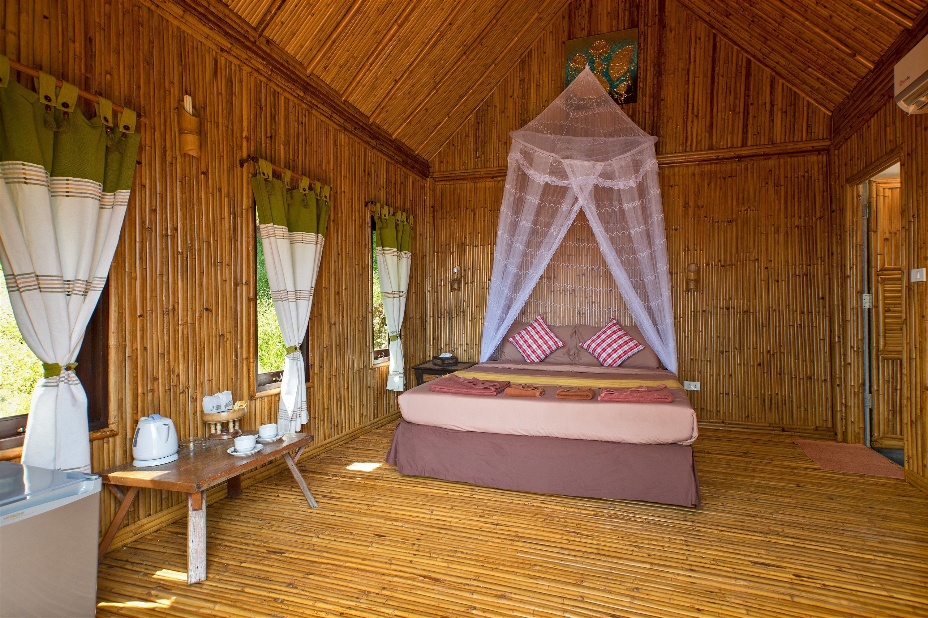 Una habitación de madera con cama, una mesa con hervidor y mosquitero.