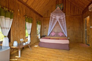 Una habitación de madera con cama, una mesa con hervidor y mosquitero.