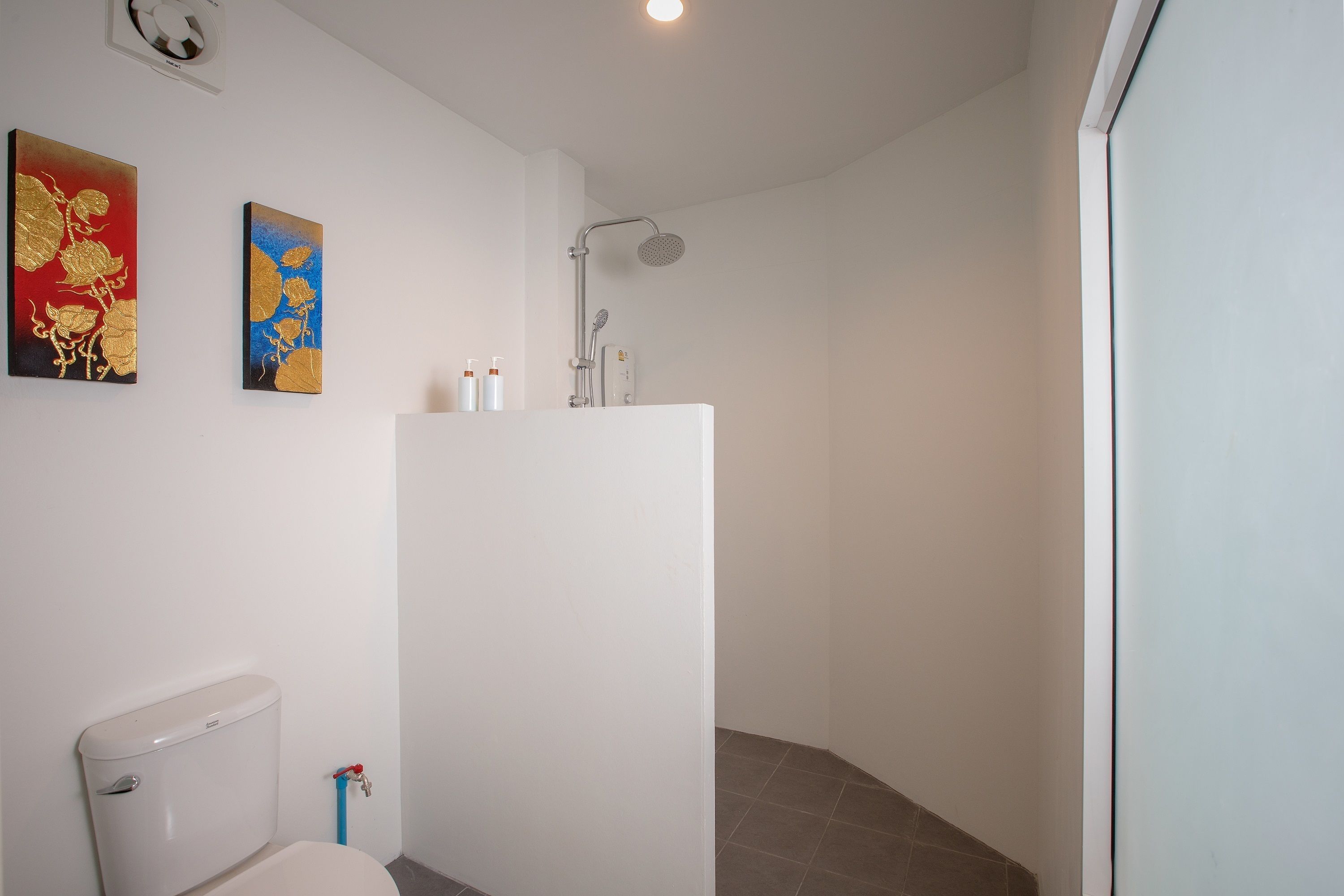 Une salle de bain équipée de toilettes, d’une douche et de deux tableaux accrochés au mur.