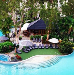 A pool area with lounge chairs, umbrellas, and a small building. - Elysium Triton by the Sea (Palm Cove)