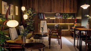 A cozy room with a sofa, chairs, a table, a lamp, and a bookshelf. - COQ Hotel Paris (Paris)