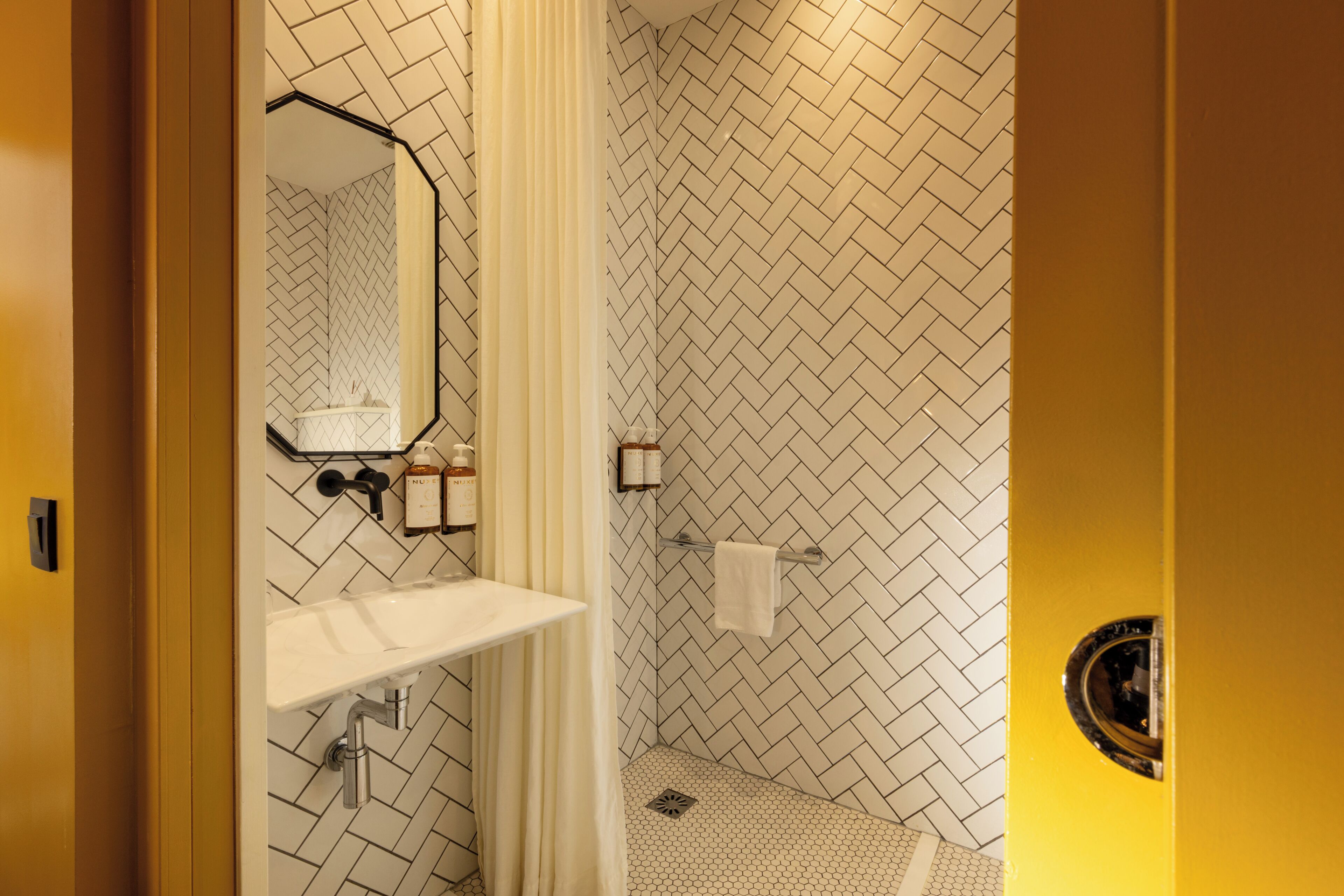Een badkamer met een witte wastafel, spiegel en douchegedeelte met een herringbone tegelpatroon.