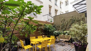 A patio with a yellow table and chairs, surrounded by potted plants and a wooden fence. - COQ Hotel Paris (Paris)