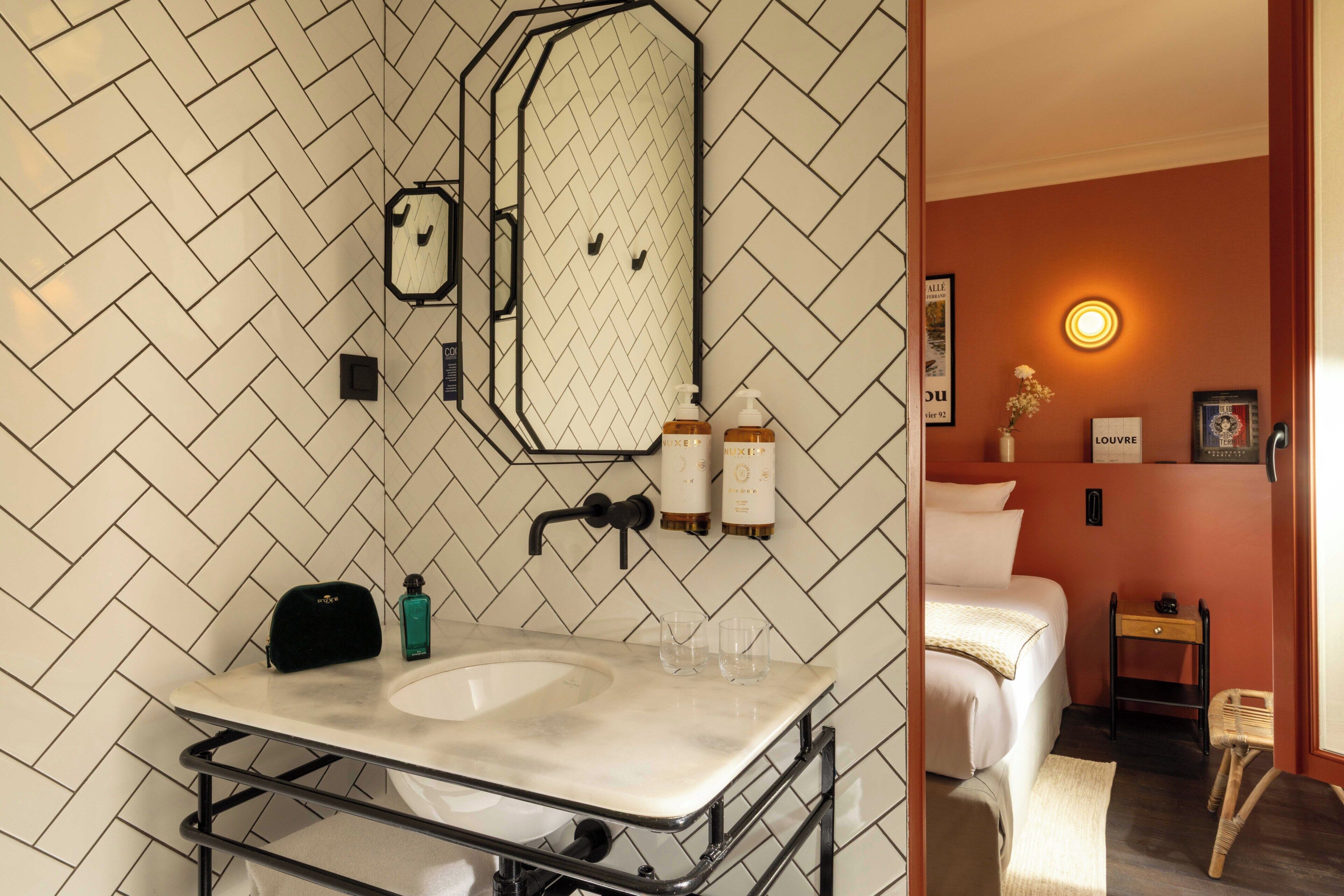 A bathroom with a herringbone tile backsplash, a mirror, a sink with a towel rack, and toiletries.