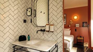 A bathroom with a herringbone tile backsplash, a mirror, a sink with a towel rack, and toiletries.