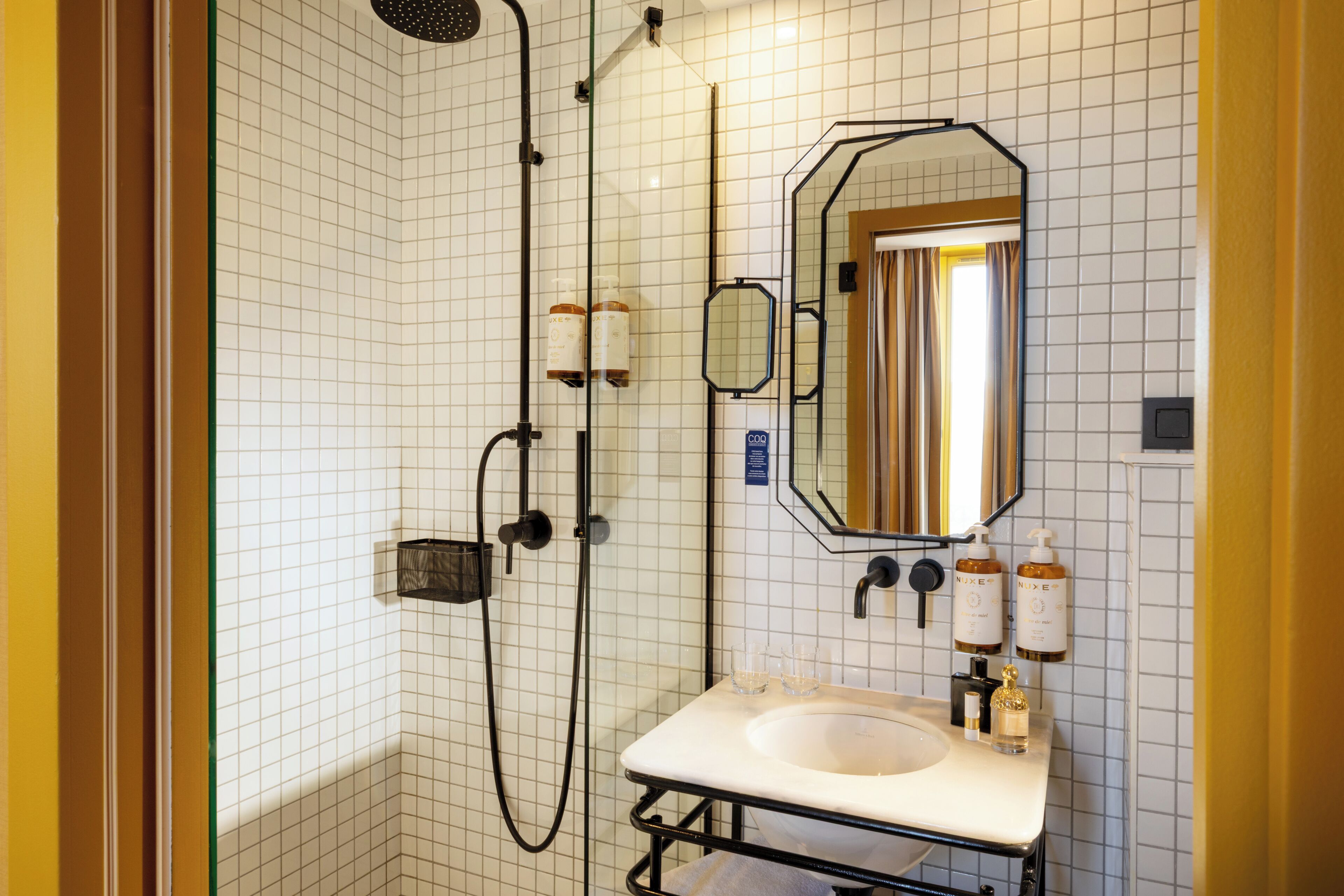 A bathroom with a shower, sink, mirror, and toiletries.